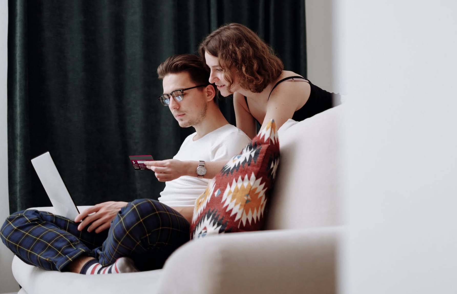 Un chico y una chica sentados en el sofa a punto de pagar con tarjeta